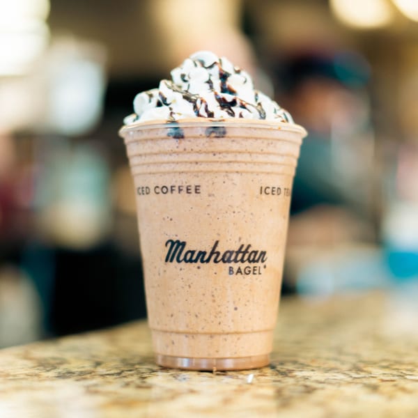 Manhattan Bagel's iced coffee drink with whipped cream and chocolate drizzle on a counter.