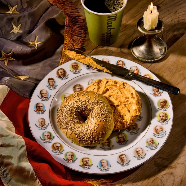 Manhattan Bagel with cream cheese on a presidential plate, coffee, and candle next to an American flag.