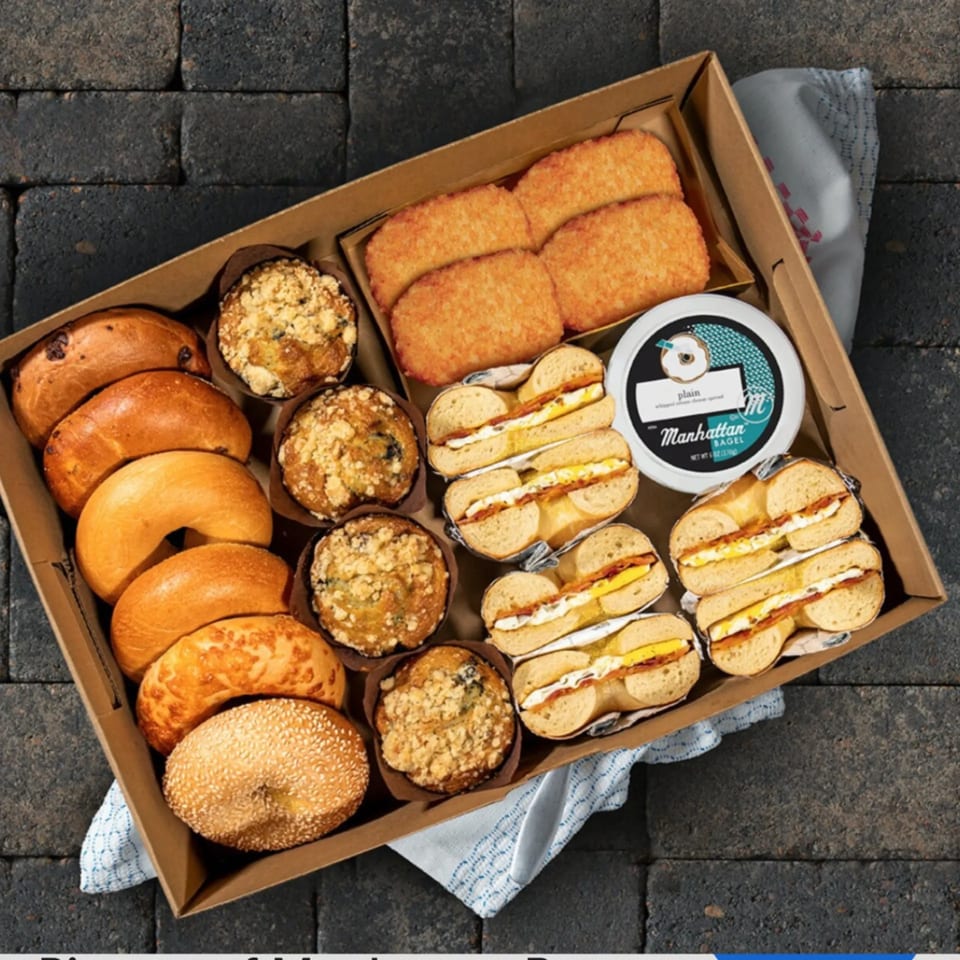 A Manhattan Bagel catering box filled with bagels, muffins, hash browns, and bagel sandwiches.