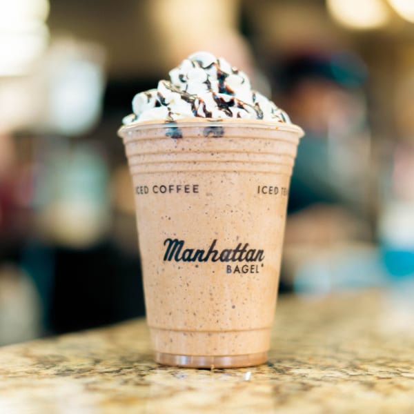 Manhattan Bagel's iced coffee drink with whipped cream and chocolate drizzle on a counter.