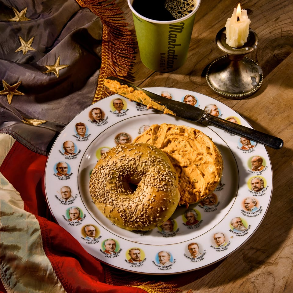 Manhattan Bagel with cream cheese on a presidential plate, coffee, candle, and American flag.