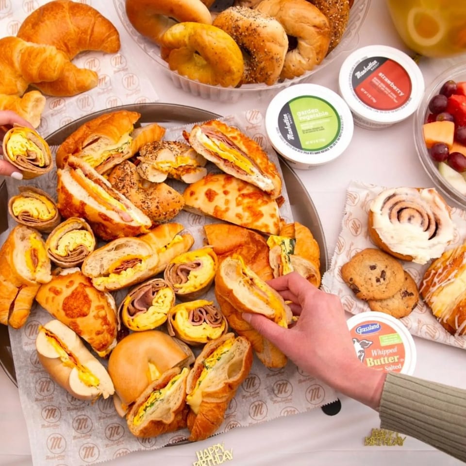 A breakfast spread with bagels, croissants, wraps, fruit, cookies, and cream cheese from Manhattan Bagels.