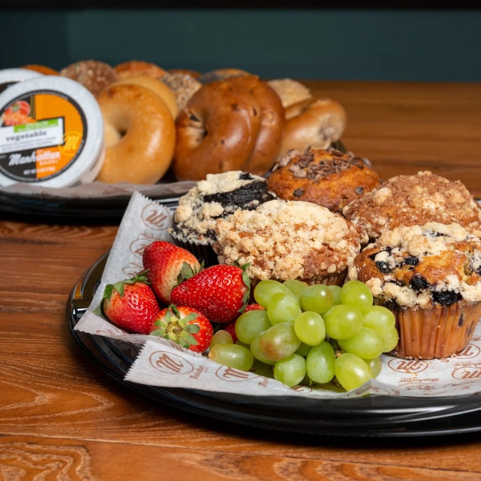 Manhattan Bagels breakfast platter with bagels, muffins, cream cheese, strawberries, and grapes.