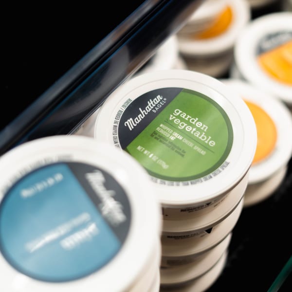 Manhattan Bagel's Garden Vegetable whipped cream cheese spread containers are stacked in a display.