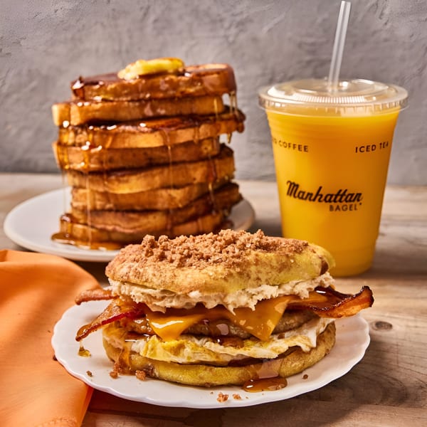 A Manhattan Bagel breakfast sandwich with bacon, egg, and cheese, next to French toast and orange juice.